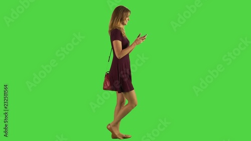 Young woman walking while texting. Happy.  Full body shot over green screen. Two takes.
