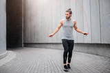 Strong and muscled young man jumping and using rope for that. He looks to left. Guy is calm and concentrated on doing excercise. He is alone there.