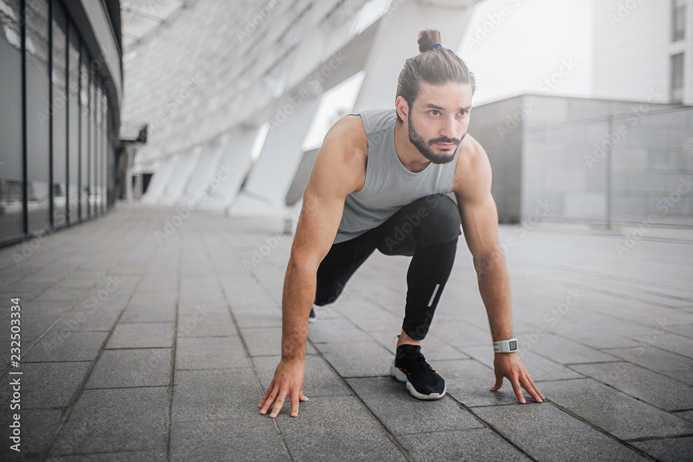 Picture of young man ready to run. He stands in sprint position and look straight forward. Guy is ready to run fast. He is strong and well-built.