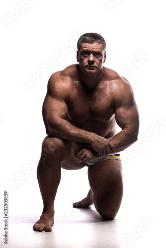 large powerful man showing his muscles in the Studio without a shirt on white background, sitting on his knee