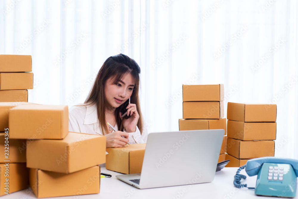 Women business owner using phone for confirm address of customer and writing in packing box at home office. online shopping SME entrepreneur or freelance working concept. Women business owner using phone for confirm address of customer and writing in packing box at home office. online shopping SME entrepreneur or freelance working concept.