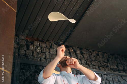 Fotografie Skilled chef preparing dough for pizza rolling with hands and throwing up