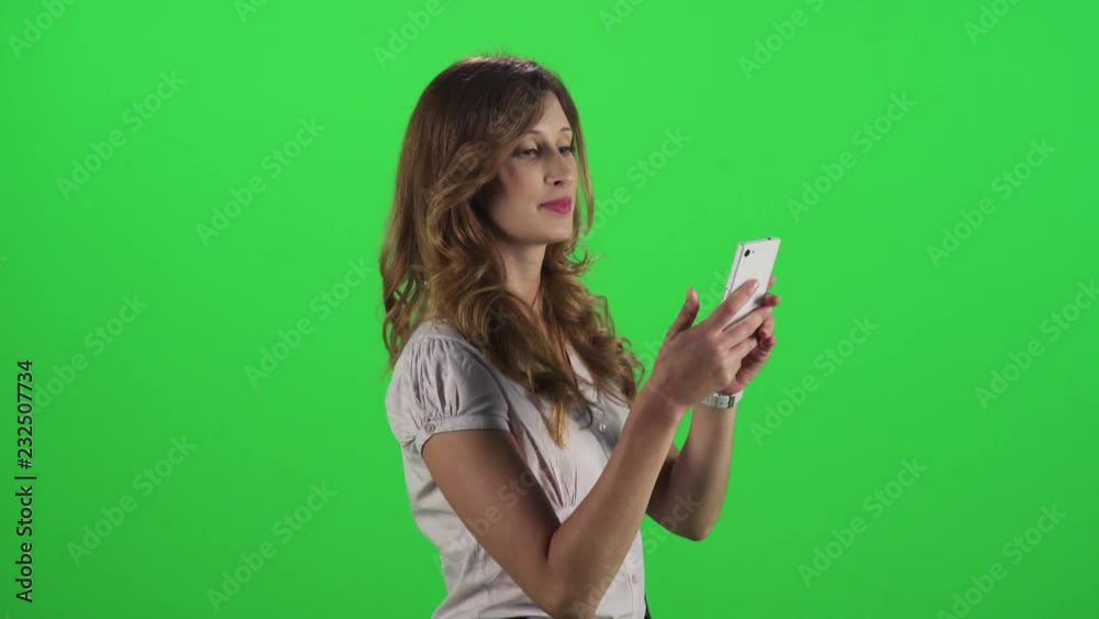 A young businesswoman walking in a medium sideways shot over a green screen, answers a call, talk and smile, hangs.