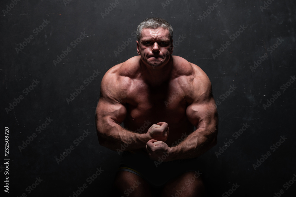large powerful man showing his muscles in the Studio without a shirt on grunge black wall