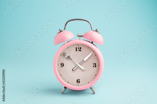 Alarm clock. Fork and knife instead of clock hands. Concept of intermittent fasting, lunchtime, diet and weight loss