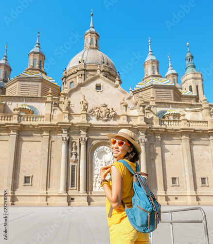 Young happy woman tourist walking near the famous cathedral Del Pilar on the central square during summer vacation in Zaragoza city, Aragon, Spain