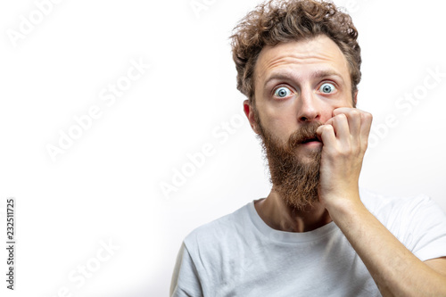Portrait of a frustrated attractive blonde man in despair after a big collapse in his life, keeps fingers near mouth dressed casually, staring at camera with horror, isolated over white background.