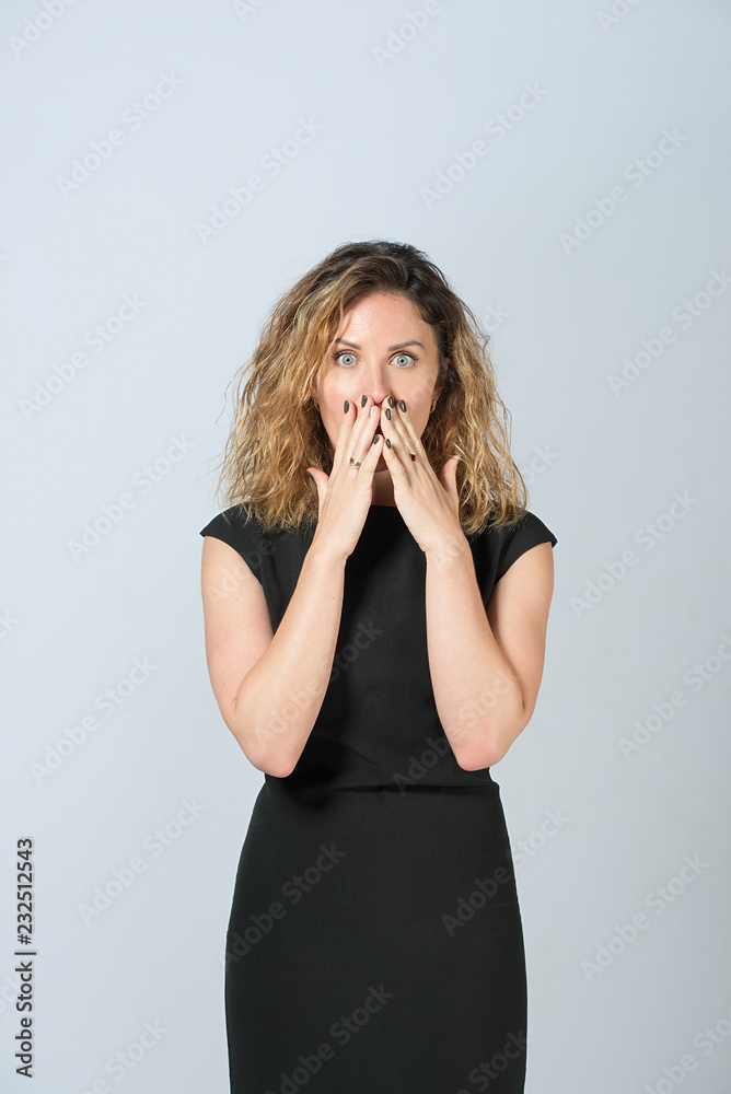 beautiful business woman in glasses in black dress on a gray background. happy face. she closed her mouth with her palms in surprise, looking at the camera. beautiful business woman in glasses in black dress on a gray background. happy face. she closed her mouth with her palms in surprise, looking at the camera.