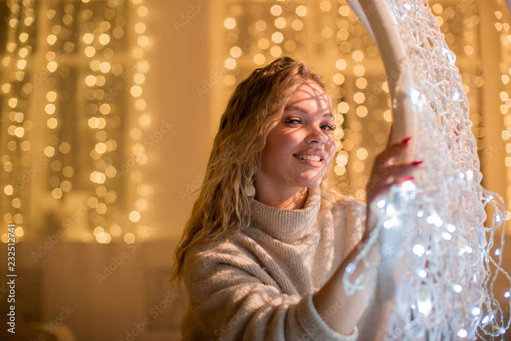 A beautiful blonde is sitting in a hanging chair on the background of Christmas garlands. A beautiful blonde is sitting in a hanging chair on the background of Christmas garlands.
