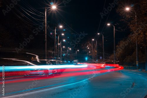 City at night with street lamp lights and cars leaving a driving trail of colorful bright headlights