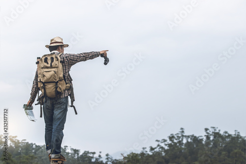 hiker with backpack standing holding map and binoculars in hands for checking on the mountain