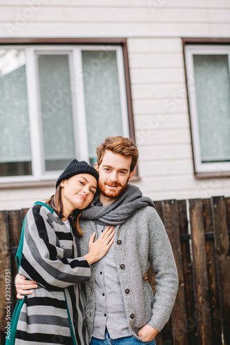 Portrait of young caucasian couple dressed in stylish warm coats standing outdoors near the modern house at the fall season © alfa27