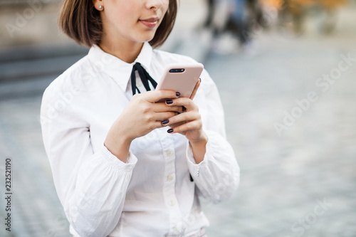Portrait of a beautiful woman using mobile phone while standing on blurred street background.