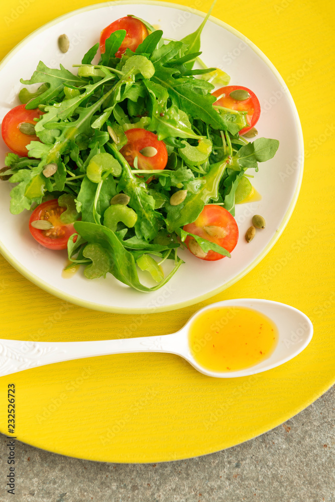 Vegetarian salad with arugula, cherry tomatoes and sunflower seeds on white ceramic plate, top view