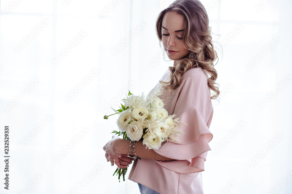 Beautiful young blonde woman with bouquet of white flowers. Portrait of pretty blonde girl in pink clothes. Florist in her work place