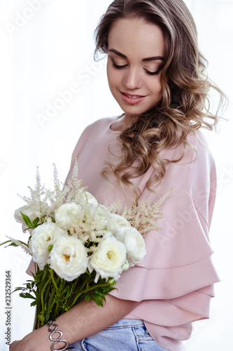 Beautiful young blonde woman with bouquet of white flowers. Portrait of pretty blonde girl in pink clothes. Florist in her work place