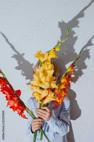 Front view portrait of unrecognizable boy hiding behind the bouquet of colorful gladiolus in direct flashlight photo