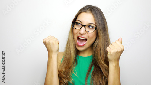 Self determined woman with glasses looking to the side with clenches fists and exclaims with triumph expression, cheers about something good, screams: Yes, I did it finally! People and body language.