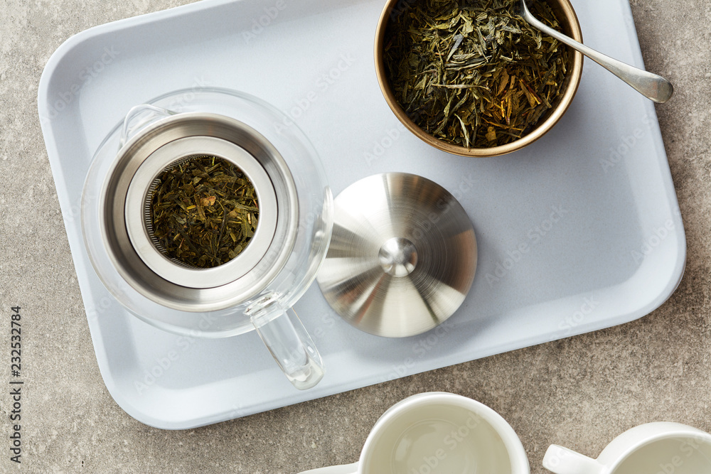 Teapot with dry fresh green tea on tray. Teapot with dry fresh green tea on tray.