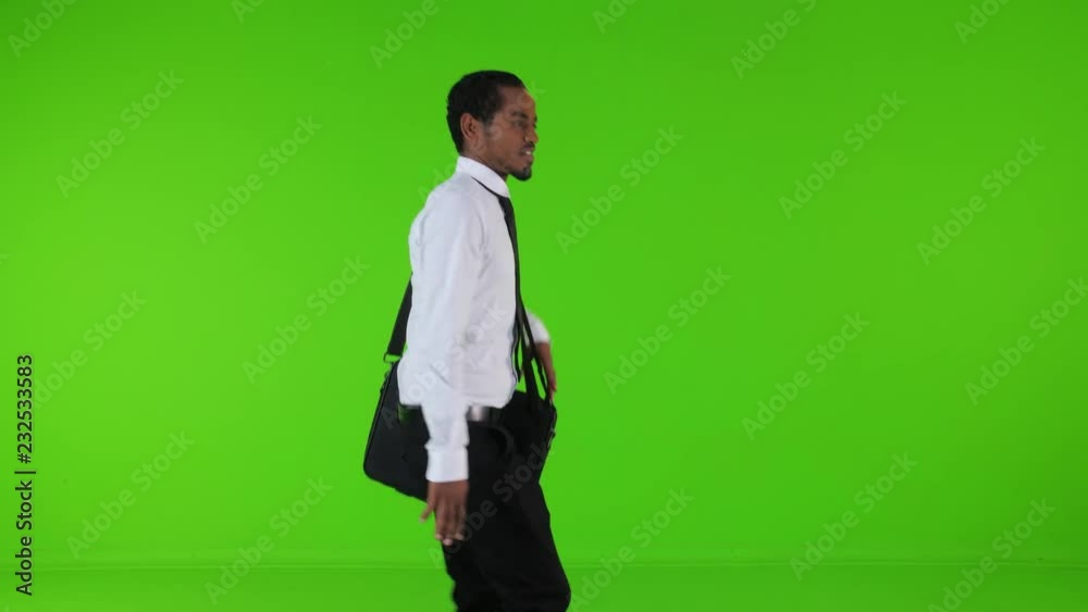 extremely Happy young businessman walking and looking around, holding a bag, over a green background, medium side shot. extremely Happy young businessman walking and looking around, holding a bag, over a green background, medium side shot.