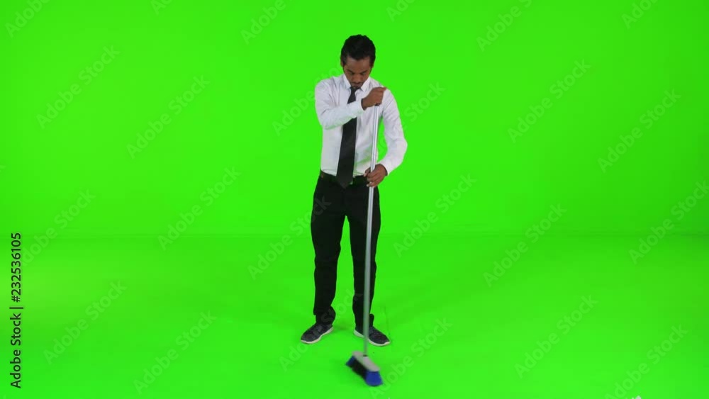 Young businessman sweeping with a broom over a green screen. Looking into the lens, long shot. Young businessman sweeping with a broom over a green screen. Looking into the lens, long shot.