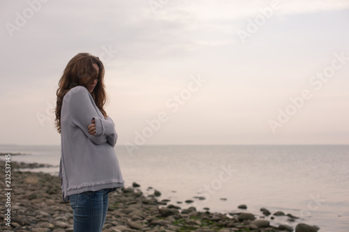 Young  Sad Pregnant Woman in a  Knitted Sweater Standing on a Deserted Beach. Sea on a Background.