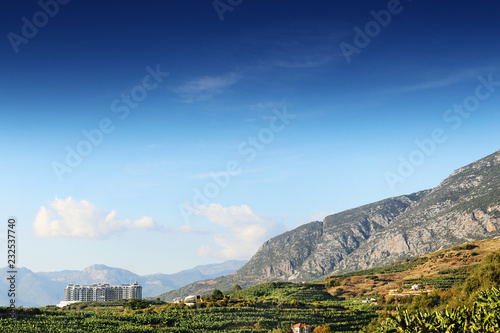 Landscape with mountains, green fields and house and blue sky