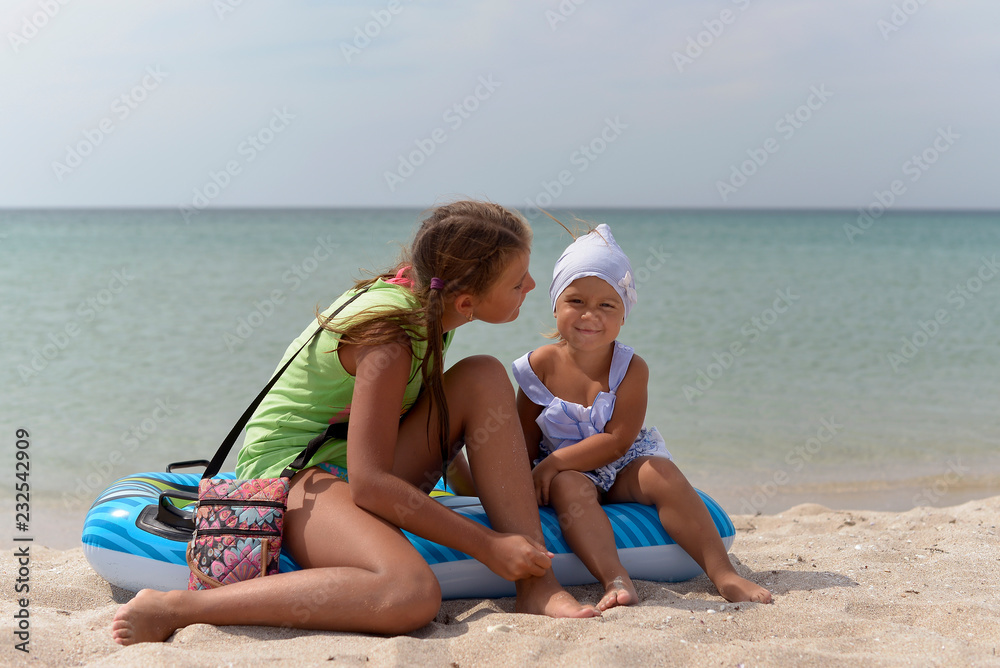Two friendly girls sisters relax on a sandy beach on a hot summer day