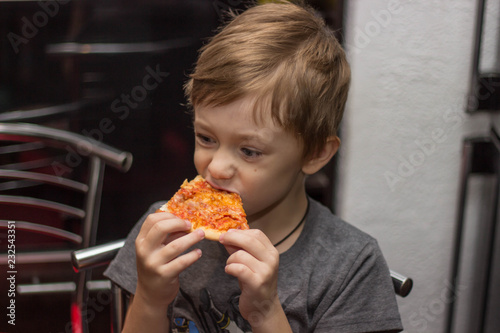 The boy eats a very tasty pizza with great pleasure.