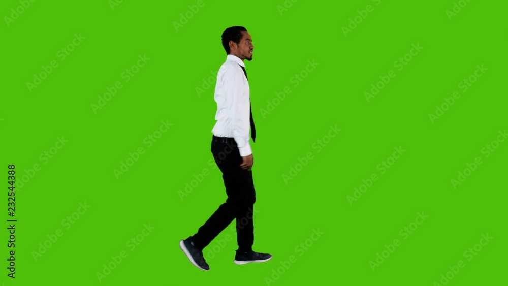 Happy young businessman walking and looking around over a green background, waving hello. Full side shot. Happy young businessman walking and looking around over a green background, waving hello. Full side shot.