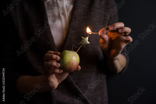 Unrecognizable person holding apple and trying to light star-shaped candle with match