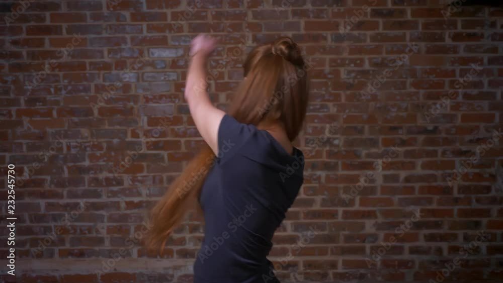 Dancing and jumping shooting of red-haired female in brick stdio, being in good mood and shape, emotionally happy, brick studio indoor