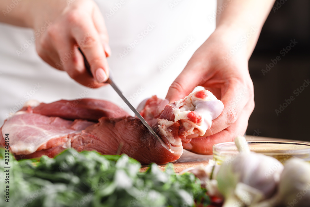 The concept of cooking meat. The chef, the butcher, cuts raw meat with beef, lamb, veal, holding a knife in his hand, on a wooden table, next to lie raw vegetable
