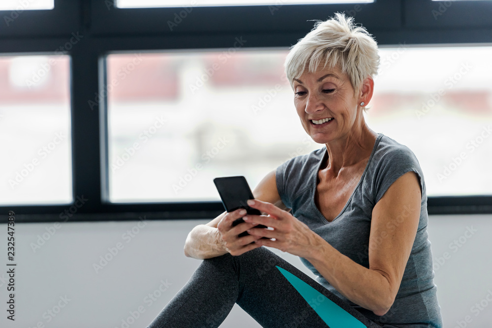 Senior active woman using smart phone at home after practicing yoga. The use of technology by the elderly. Senior active woman using smart phone at home after practicing yoga. The use of technology by the elderly.