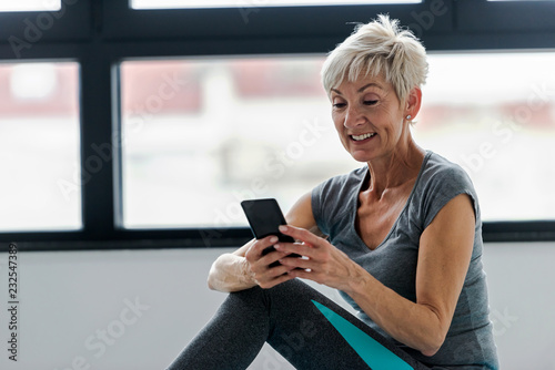 Senior active woman using smart phone at home after practicing yoga. The use of technology by the elderly.