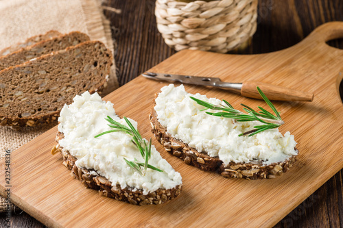 Whole grain bagels with cream cheese on wooden board, selective focus