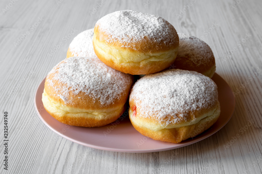 Homemade sweet donuts with powdered sugar on pink plate on white wooden table, side view. Closeup.