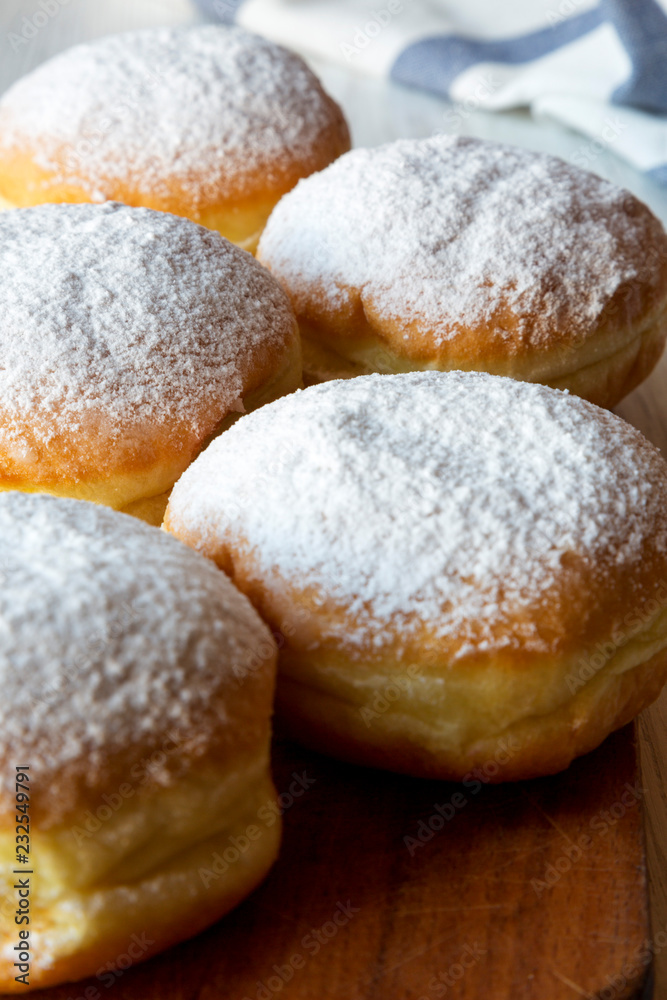 Homemade sweet donuts with powdered sugar on rustic wooden board on white wooden background, side view. Close-up.