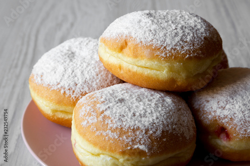 Homemade sweet donuts with powdered sugar on pink plate over white wooden background, side view. Close-up.