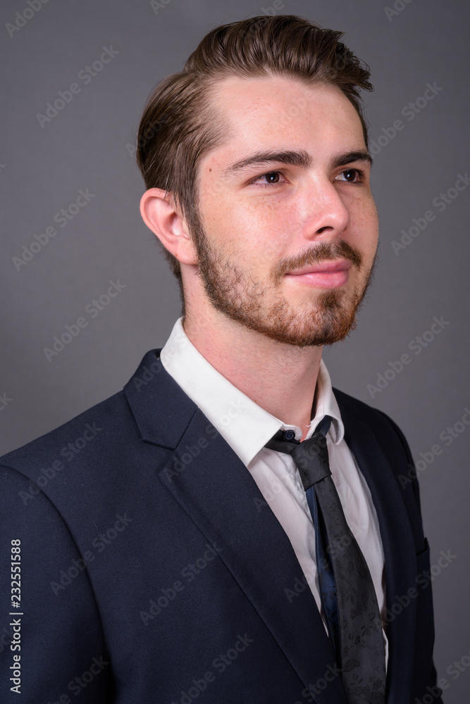 Young handsome bearded businessman against gray background