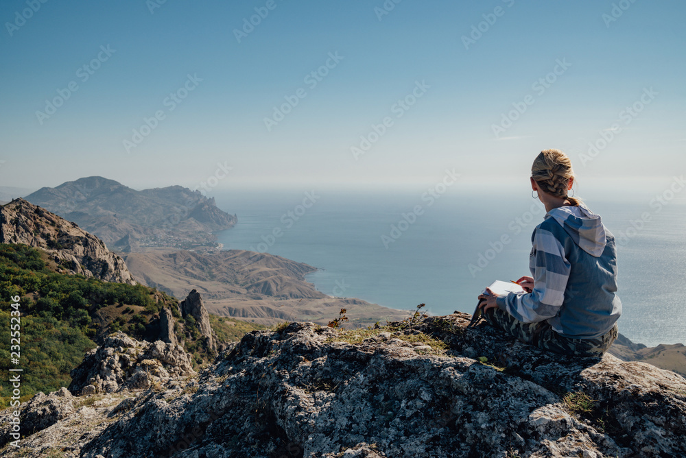 Young girl draws in a sketchbook on top of a mountain Young girl draws in a sketchbook on top of a mountain