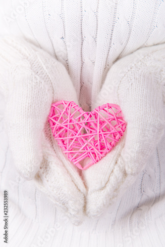 Hands in white knitted mittens holding pink wicker heart.