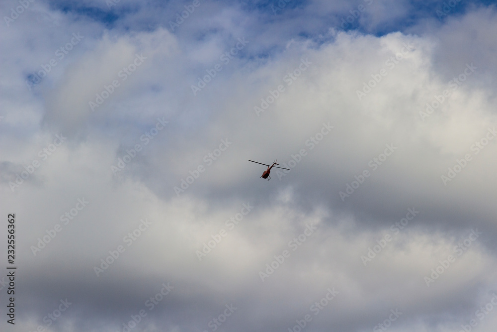 Red helicopter high in the blue sky with white clouds