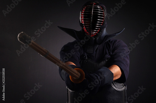 Kendo fighter holding and training with bamboo sword in studio on black background.