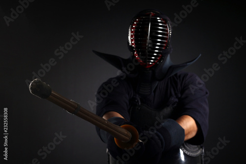 Kendo fighter holding and training with bamboo sword in studio on black.
