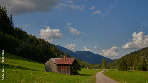 Berghütte mit einer Wiese vor den Bergen mit weiblauem Himmel