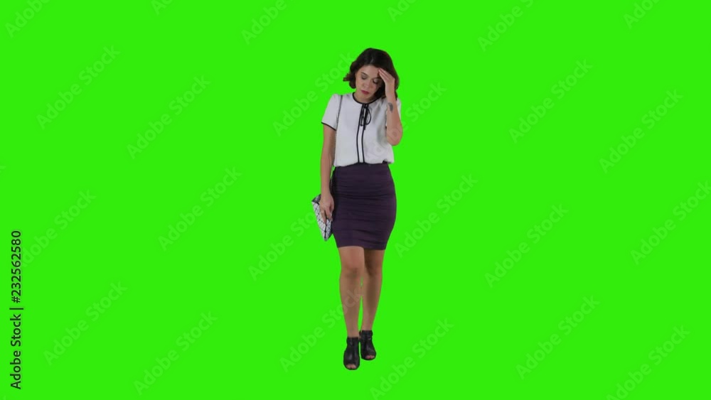 Stylish sad woman walking while having a headache over a green screen in a full frontal shot. Stylish sad woman walking while having a headache over a green screen in a full frontal shot.