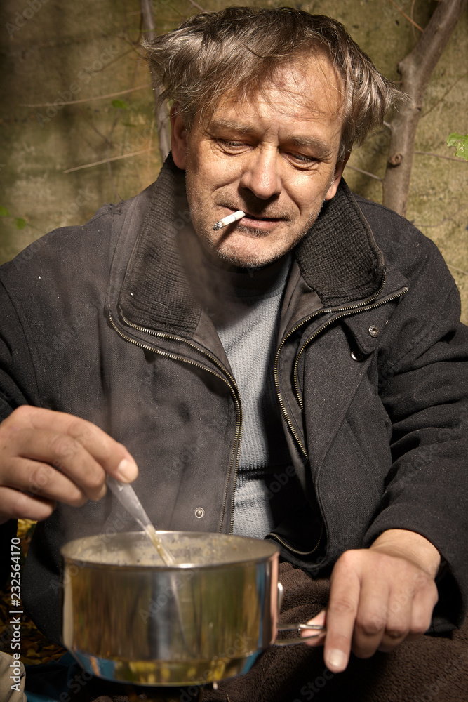 Ugly pauper man living outdoor preparing and eating lentil soup Ugly pauper man living outdoor preparing and eating lentil soup