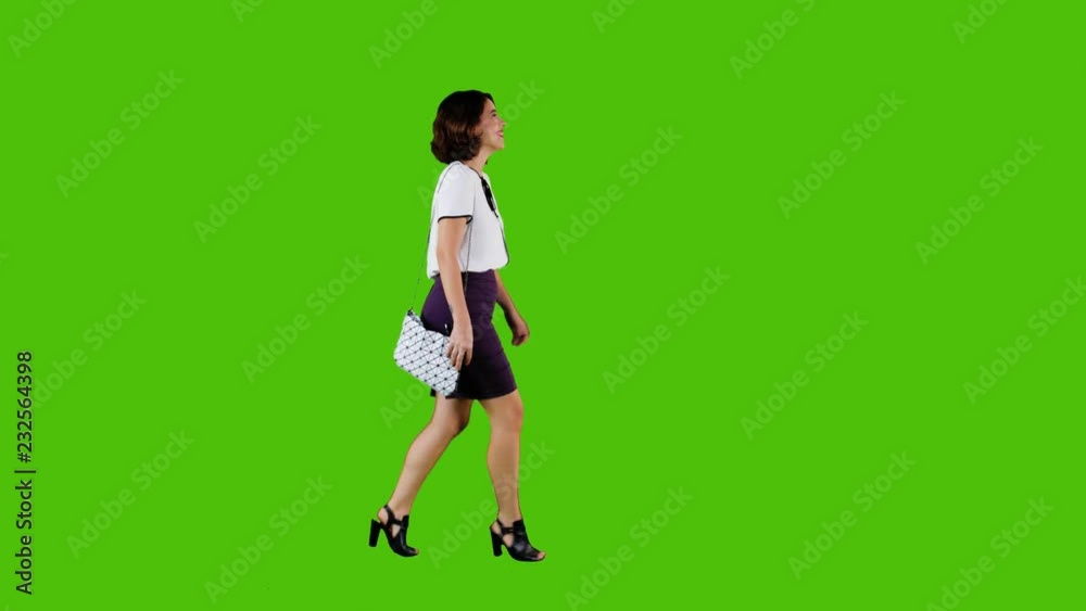Stylish happy woman walking and smiling over a green screen in a full side shot. Stylish happy woman walking and smiling over a green screen in a full side shot.
