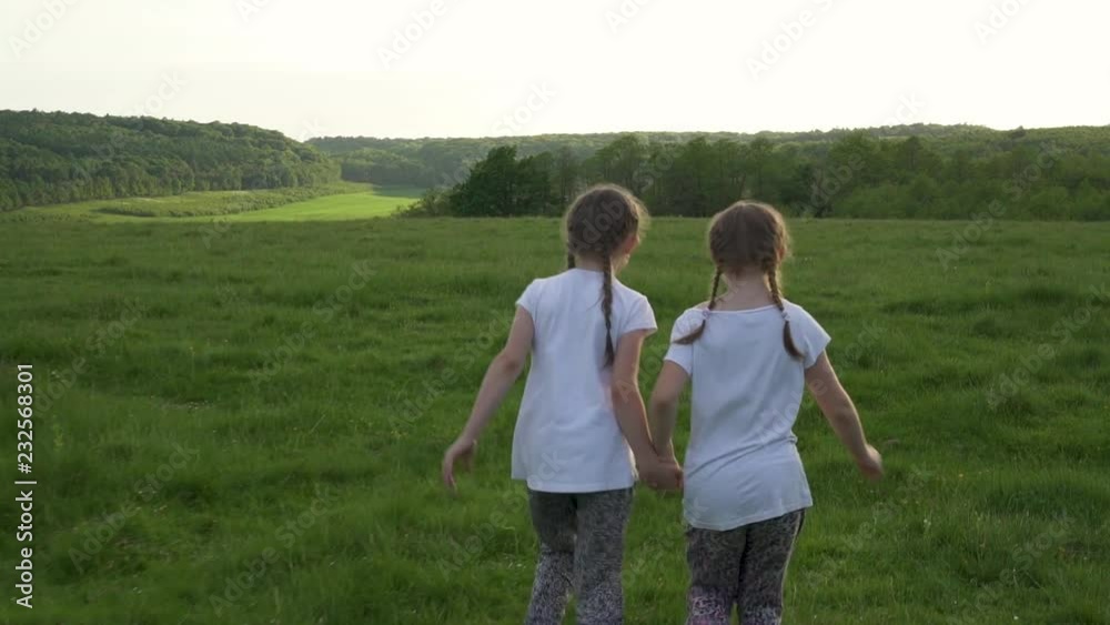 Two sisters running away in meadow and laughing Two sisters running away in meadow and laughing